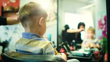 Hairdresser cutting childs hair while he playing with a toy video