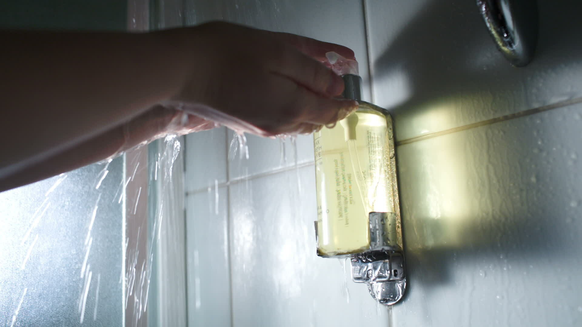 Hands pushing a container with soap under shower stream