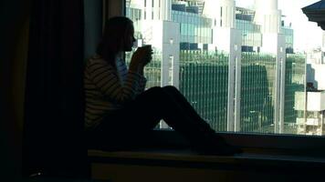 vrouw drinken koffie Aan de vensterbank met stad visie in venster video