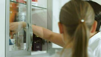 Cosmetician taking cosmetic from cabinet and showing it her colleague video