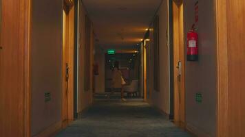 un' Hotel visitatore passeggiate giù un' corridoio pieno di giallo luci guardare per un' camera video
