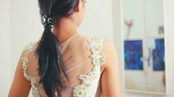 un asiatico donna nel un' molto elegante bianca vestito è guardare nel il specchio mentre provando su il vestito video