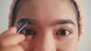 un hermosa asiático mujer es haciendo maquillaje me gusta delineador de ojos y rojo lápiz labial en su cara en frente de el vendaje mesa video