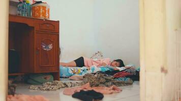 un asiático mujer dormido en un cama lleno de ropa dispersado en su habitación video