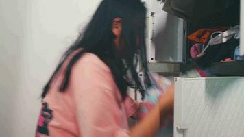 un asiático mujer es mirando para ropa en un prisa en su guardarropa video