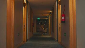 uma hotel Visitante anda em baixa uma corredor cheio do amarelo luzes olhando para uma quarto video