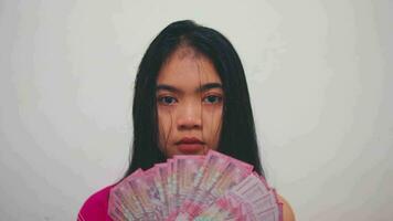 an Asian woman with black hair holding a lot of money with a very sad expression in her room video