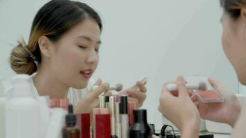 Beautiful Asian woman sit in front of a mirror and smile on makeup. face of a healthy woman applying makeup. Advertisement, lifestyle , cosmetics, makeup accessories, beauty activity, beautician video