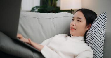 Asian woman using a laptop computer while lying on the sofa photo