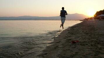 hombre corriendo a lo largo un playa a puesta de sol video