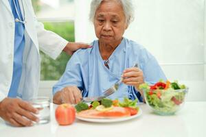 Asian elderly woman patient eating salmon stake and vegetable salad for healthy food in hospital. photo