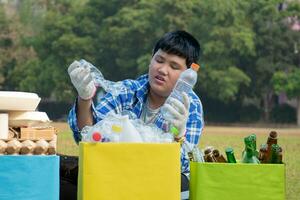 Asian boy in plaid shirt sitting on playground of school with various boxes of separated garbabes or trashes inside, concept for eco friends and global warming campaign, soft and selective focus. photo