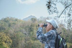 Asian boy in plaid shirt and cap doing the summer activity at local national park by watching birds, fish, insects, animals, trees, flower by using map and binoculars, soft and selective focus. photo