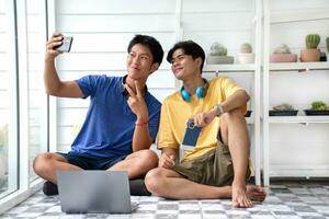 Young asian gay couple spending their free time, making selfie and looking after cactus pots on shelves behind by using magnifying glass, LGBT lover special recreational activity concept. photo