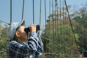 asiático Niños sostiene prismáticos y local nacional parque mapa, descansando y leyendo información en mapa cerca honda puente de local nacional parque durante naturaleza y verano acampar de a ellos, adolescentes' actividad concepto. foto