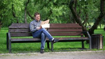 hombre lee periódico en banco en el parque 1 video