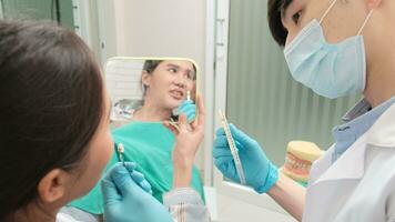 asiatisch männlich Zahnarzt erklärt kieferorthopädisch Pflege und Bleaching zu ein jung weiblich geduldig mit implantieren Prothese Farbe Schatten im Dental Klinik, Zähne Hygiene, und Fachmann Gesundheitswesen Arzt im ein Krankenhaus. video
