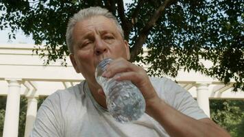 A sporty elderly caucasian man drinks water after fitness classes video