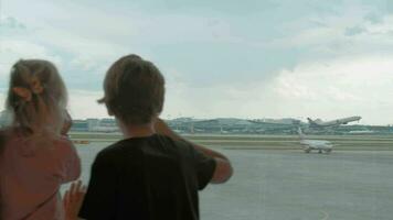 kinderen aan het wachten Bij de luchthaven en aan het kijken vliegtuigen van de terminal video