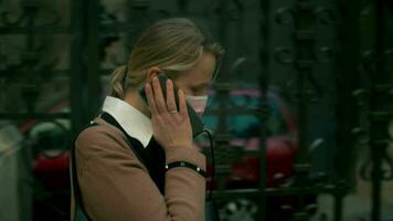 vrouw in masker pratend Aan mobiel wanneer wandelen in de stad video