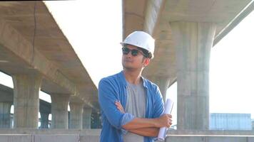 Asian engineer worker in protective helmet and blueprints paper on hand inspecting construction project a road expressway that is done at construction site. photo