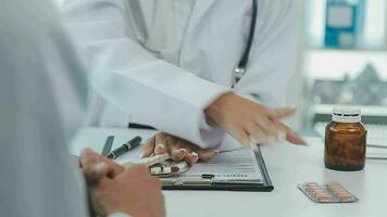 profesional hembra médico sonrisas y muestra positivo examen resultados a joven, alegre hombre. elegante, contento chico con lentes a del doctor cita en moderno oficina de médico institución. video