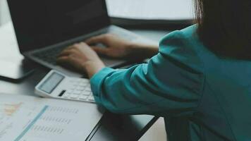 hermosa joven y sonriente mujer de negocios asiática que trabaja en una laptop y bebe café, una mujer de negocios de asia que trabaja con finanzas de documentos y una calculadora en su oficina. video