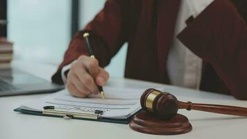 concetto di giustizia e diritto. giudice maschio in un'aula di tribunale con il martelletto, lavorando con computer e tastiera docking, occhiali, sul tavolo alla luce del mattino video