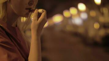 Woman applying lipgloss outside at night video