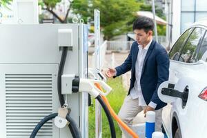 A man attaching power cable to electric car. Electric vehicle Recharging battery charging port. Concept of green energy and reduce CO2 emission. EV car. photo