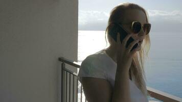 A woman on a balcony talking to a phone and a sea view behind her video