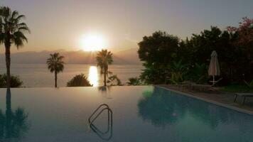 Vacation scene with swimming pool overlooking sea and mountains at sunset video