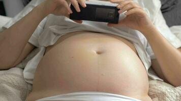 zwanger vrouw met kaal buik resting Bij huis en gebruik makend van mobiele telefoon video