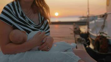 moeder verpleging en strelen baby zittend Aan de pier Bij zonsondergang video