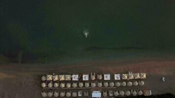 Beach with sunbeds and people swimming to the shore, aerial video