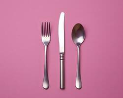 a fork spoon and knife on a pink background generative ai photo