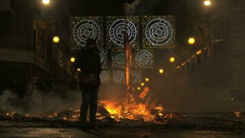 A female figure standing next to the dying bonfire on the Falles night video