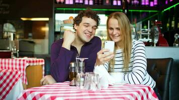 joven Pareja en café teniendo un vídeo charla en teléfono inteligente video