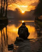 a person sitting on the side of a river at sunset generative ai photo