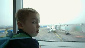 pequeño chico mirando fuera ventana y señalando a avión video