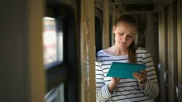 Young woman with pad standing by the window in train hallway video