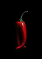 there is a red pepper that is sitting on a black surface. generative ai. photo