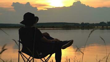 Silhouette of Young Man Who Sits in a Folding Chair on River watching sun rise. Drinking coffee,coffee ground, Travel Lifestyle success concept adventure vacations outdoor freedom emotions. photo