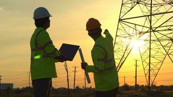 Silhouette of engineer Teams looking discussing plan. Two engineer standing on field with electricity towers at sunset. photo