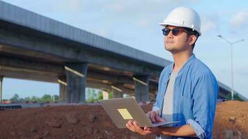 Asian civil engineer using laptop is inspecting construction project a road expressway that is done at construction site. photo