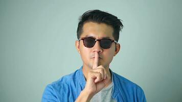 Asian man handsome wearing sunglasses asking to be quiet with finger on lips. Silence and secret concept. photo