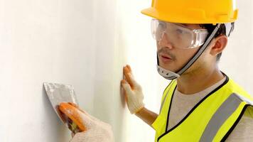 asiático construcción trabajador, espátula en mano en contra el antecedentes de un blanco muro, trabajo yesero. masilla paredes con su propio manos foto