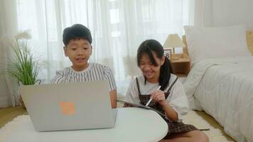 Boy using laptop looking at girl using pen write tablet in bedroom. photo