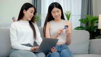 Two asian women using online shopping credit cards via their laptops on sofa at home. Online success buy sale. photo