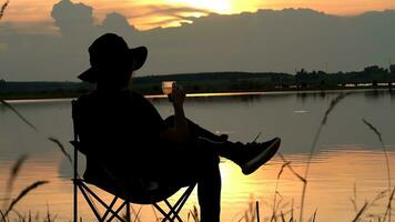 Silhouette of Young Man Who Sits in a Folding Chair on River watching sun rise. Drinking coffee,coffee ground, Travel Lifestyle success concept adventure vacations outdoor freedom emotions. photo